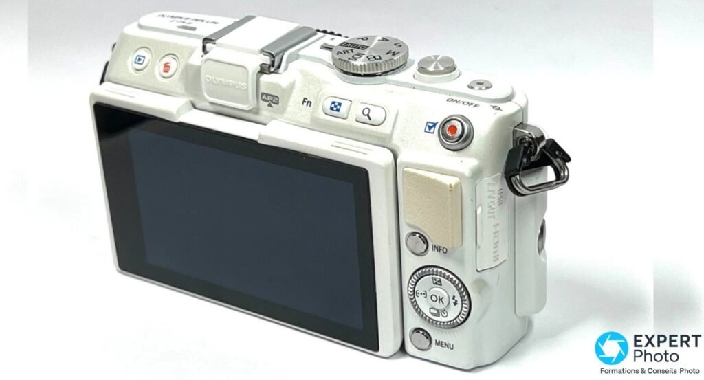 Olympus PEN E-PL6 blanc vu de dos en trois quarts droit, LCD éteint, molette PASM et bouton enregistrement visibles 