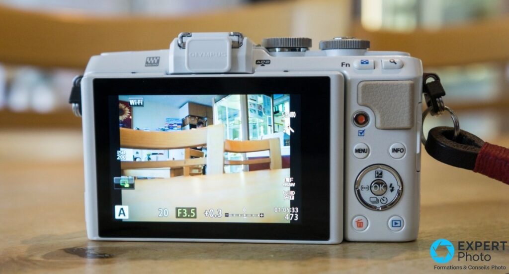 Dos du boîtier Olympus PEN E-PL7 blanc, écran LCD allumé en live view, commandes MENU INFO OK visibles, griffe flash fermée