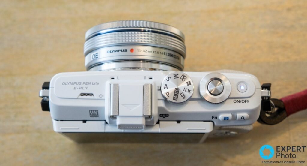 Olympus PEN Lite E-PL7 blanc vu de dessus, molette de modes P A S M iAuto ART SCN, objectif zoom 14-42mm EZ en place