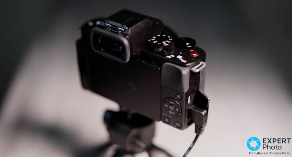 Panasonic Lumix G100 tenu d'une main en position selfie, écran orientable montrant détection de visage et f/3.5 affiché