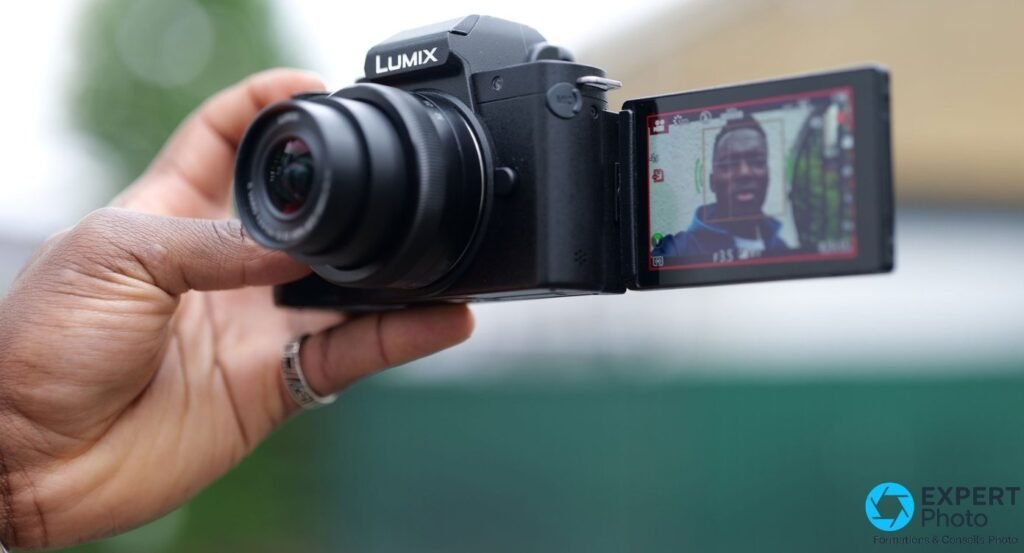 Panasonic Lumix G100 posé sur poignée-trépied Panasonic DMW-SHGR1, écran latéral déployé, ambiance studio sombre