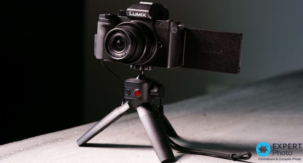 Panasonic Lumix G100 avec objectif 12-32 mm tenu d'une main, écran tactile orientable déployé sur le côté