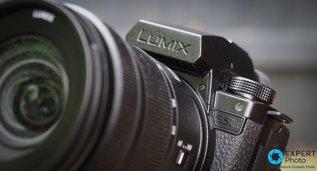 Gros plan : logo LUMIX gravé sur la bosse du viseur, molette crantée et badge S5IIx du boîtier noir, profil avec objectif.