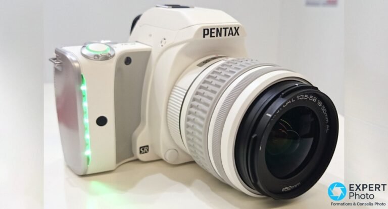 Boîtier Pentax K-S1 blanc vue 3/4 avant, LED vertes allumées sur la poignée et zoom SMC Pentax DAL 18-55mm AL monté.