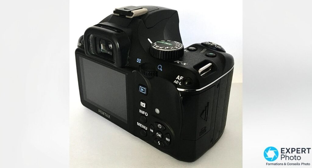 Pentax K-x en trois quarts arrière droit, molette des modes AUTO PICT, interrupteur ON/OFF et déclencheur vert.