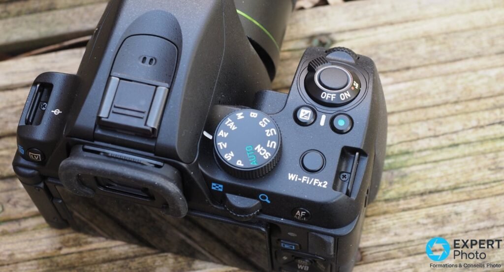 Pentax KF vue rapprochée sur la molette de modes (M, TAv, Av, Tv, P, AUTO, SCN), switch ON/OFF, bouton Wi-Fi/Fx2