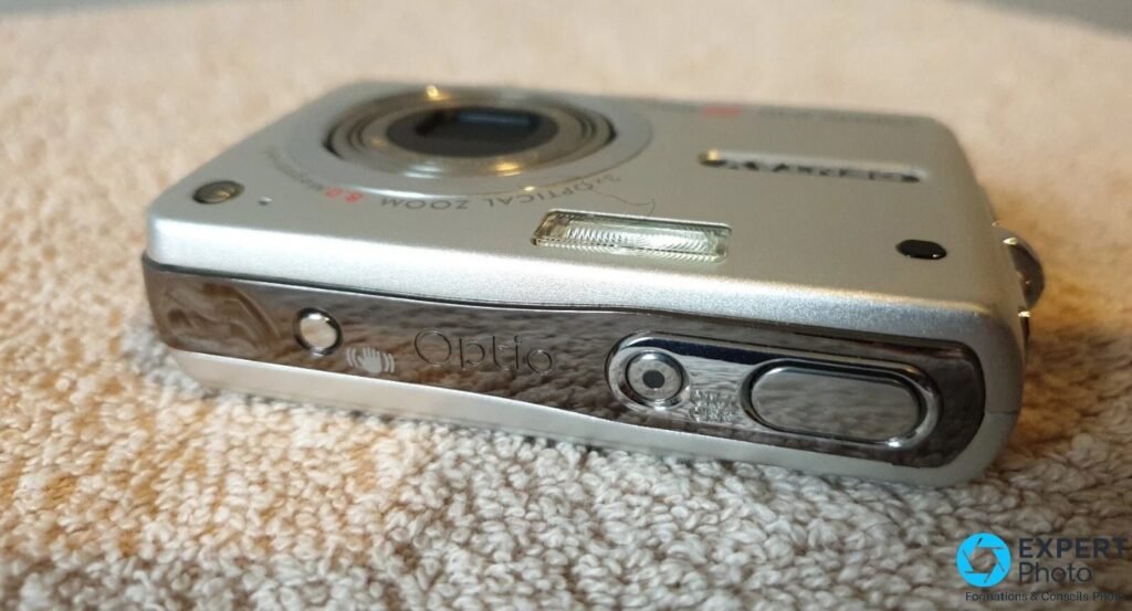 Pentax Optio A10 vu en plongée basse, objectif sorti et inscription Optio gravée sur la tranche latérale.