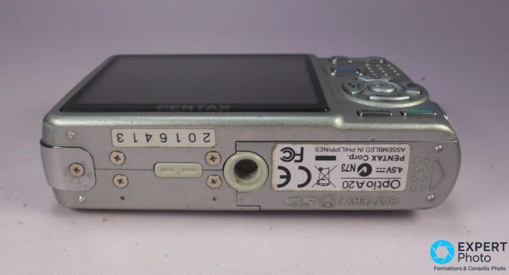 Pentax Optio A20 silver vu de dessous, étiquette produit Optio A20, numéro de série visible, pas de vis trépied. 
