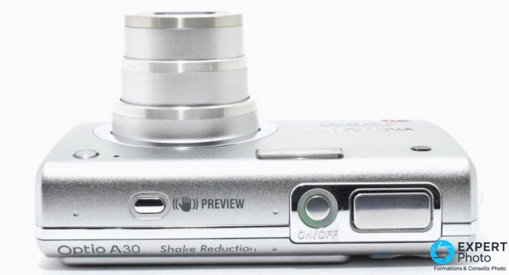 Pentax Optio A30 vu de dessus, objectif zoom déployé, déclencheur, bouton ON/OFF et pictogramme Shake Reduction