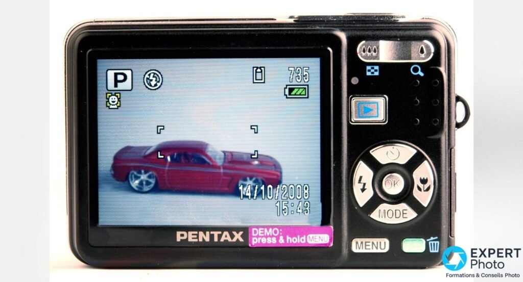 Pentax Optio A40 vu de dos, écran LCD actif affichant une voiture rouge en mode P, bandeau DEMO, pavé directionnel MENU. 