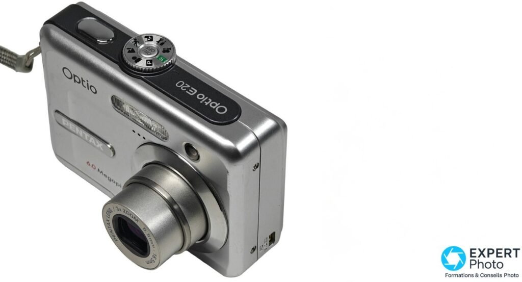 Pentax Optio E20 vu de trois quarts dessus, molette de sélection des modes et objectif 3x zoom en position sortie