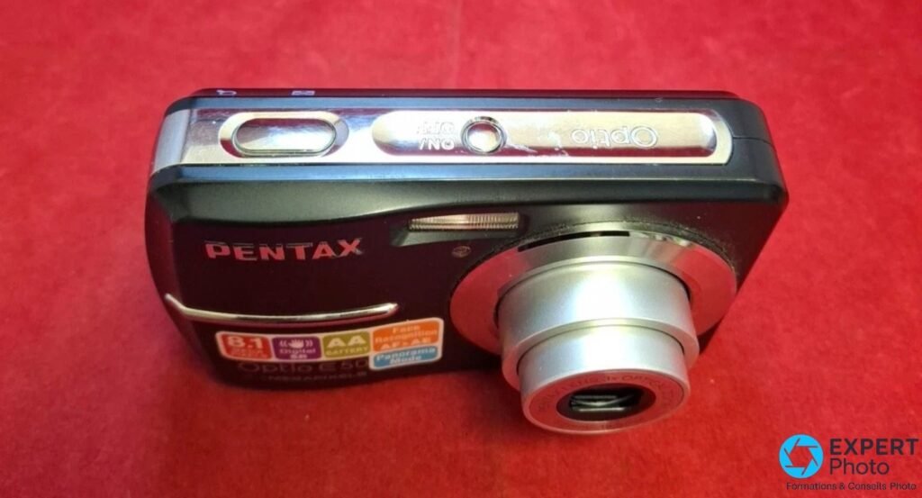  Pentax Optio E50 vue trois quarts avant, objectif zoom 3x déployé en fonctionnement, bouton ON/OFF et déclencheur visibles 