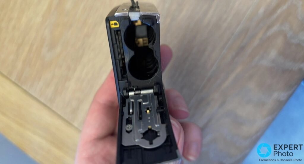 Compartiment piles AA du Pentax Optio E60 ouvert, boîtier tenu en main, fente carte SD et contacts dorés visibles