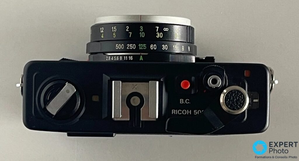  Vue du dessus du Ricoh 500 ME, bagues de vitesses et d ouverture f/2,8 à f/16, griffe flash et déclencheur rouge. 