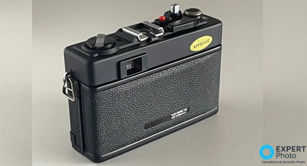 Dos du Ricoh 500 ME fermé, étiquette APPROVED jaune en haut à droite, oeilleton du viseur arrière au centre. 