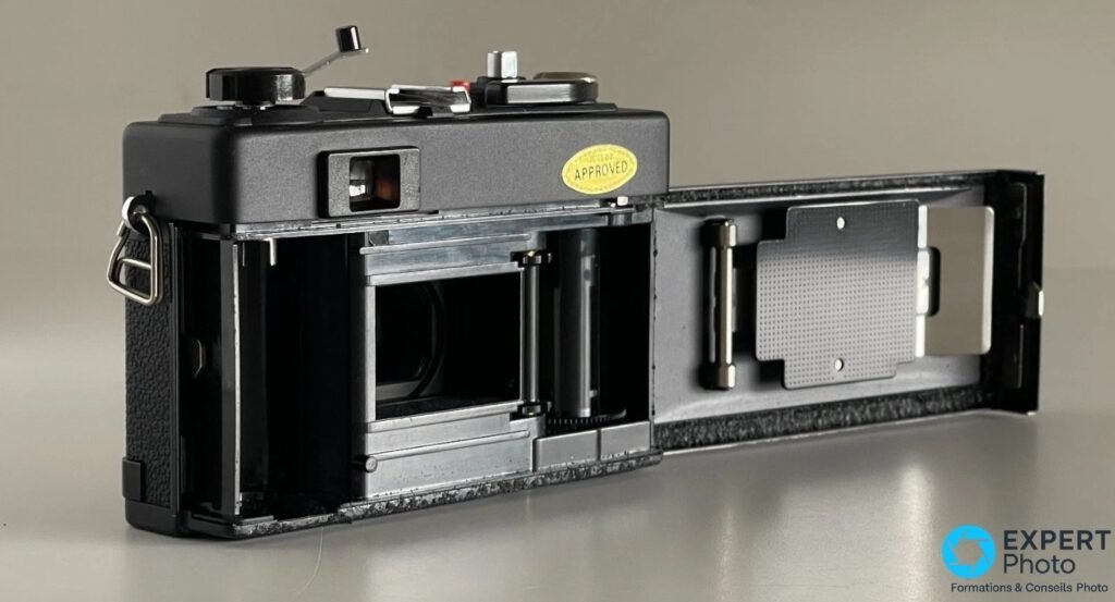  Ricoh 500 ME dos ouvert, plaque-presseur métallique et chambre film vide visibles, étiquette APPROVED en haut droit.