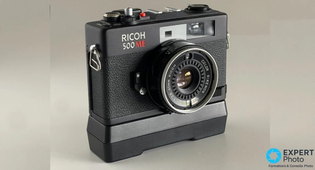 Compact télémétrique Ricoh 500 ME noir, vue en trois-quarts avant, objectif Color Rikenon 40 mm f/2,8 visible, sur support. 