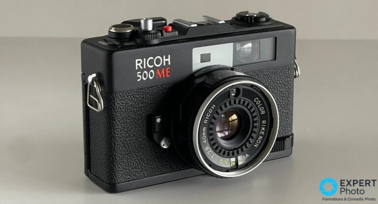 Compact télémétrique Ricoh 500 ME noir, vue de trois-quarts avant, objectif Color Rikenon 40 mm f/2,8, fond gris clair.