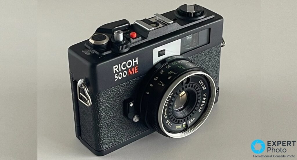 Ricoh 500 ME, trois-quarts avant, bague de distance graduée et bague de vitesses visibles sur l objectif Color Rikenon.