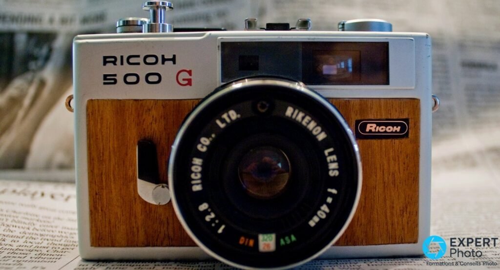 Ricoh 500G en variante placage bois vu de face, objectif Rikenon 40 mm f/2,8, posé sur journal.