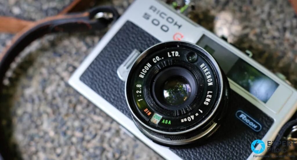 Gros plan plongée sur l'objectif Rikenon 40 mm f/2,8 du Ricoh 500G, graduations ASA et DIN visibles.