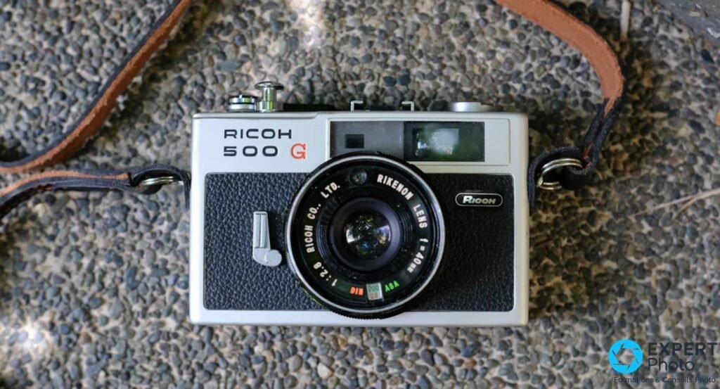  Ricoh 500G vu en plongée verticale avec objectif Rikenon 40 mm f/2,8, sangle cuir noir et marron traversante.