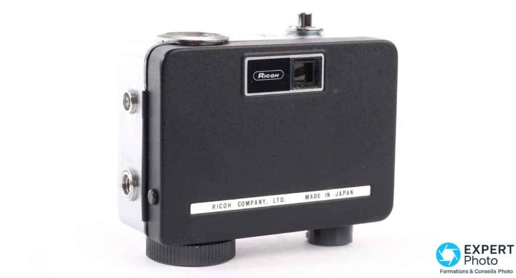 Ricoh Auto Half E vu de dos sur fond blanc, viseur, logo Ricoh gravé et mention Made in Japan visibles. 