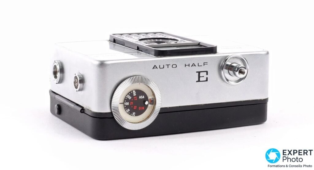 Ricoh Auto Half E vu en plongée latérale, gravure AUTO HALF E et molette de sensibilité ASA/DIN visibles.
