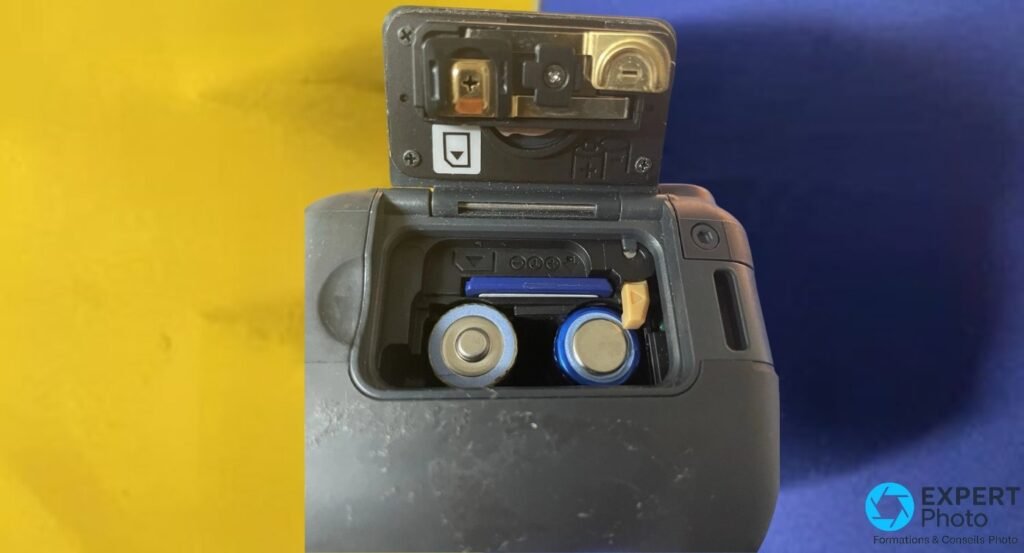 Compartiment batterie du Ricoh Caplio 500SE ouvert avec deux piles AA insérées et une carte SD bleue.