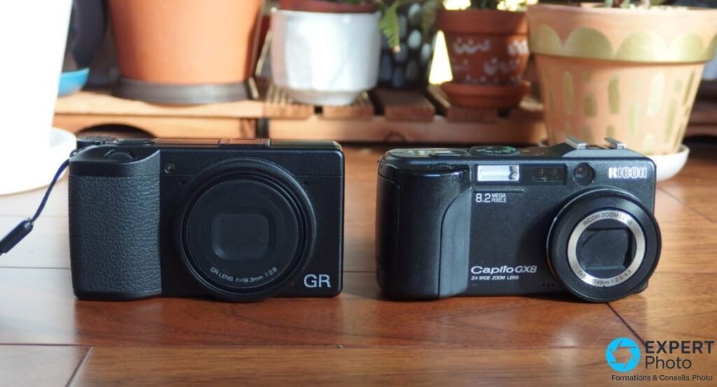 Ricoh GR Digital à gauche et Ricoh Caplio GX8 à droite, vues de face sur table en bois, plantes en arrière-plan.