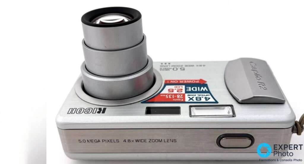 Ricoh Caplio R2 sur le dos avec objectif zoom 4,8x déployé en téléobjectif sur trois sections argentées télescopiques. 