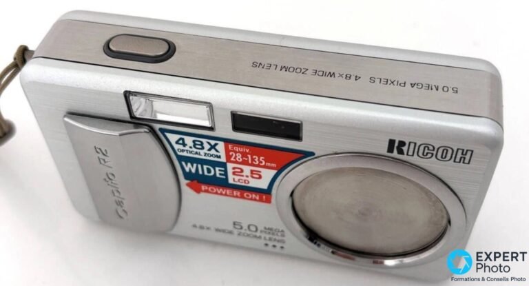 Ricoh Caplio R2 en 3/4 face avec cache d'objectif fermé, déclencheur sur le dessus et sticker d'origine bien visibles.