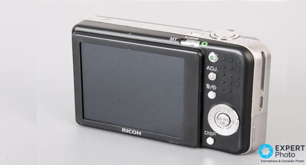 Ricoh Caplio R6 noir vu de trois quarts arrière, écran LCD 2,7 pouces, bouton ADJ et pad MENU OK.