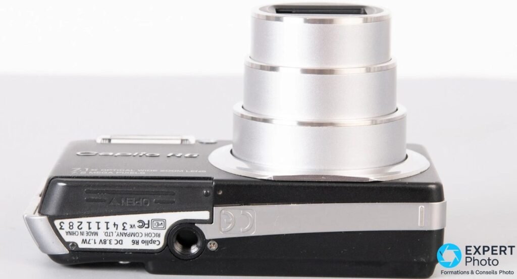 Ricoh Caplio R6 noir vu de dessous, étiquette constructeur Ricoh, marquage Made in China, vis 1/4 trépied. 