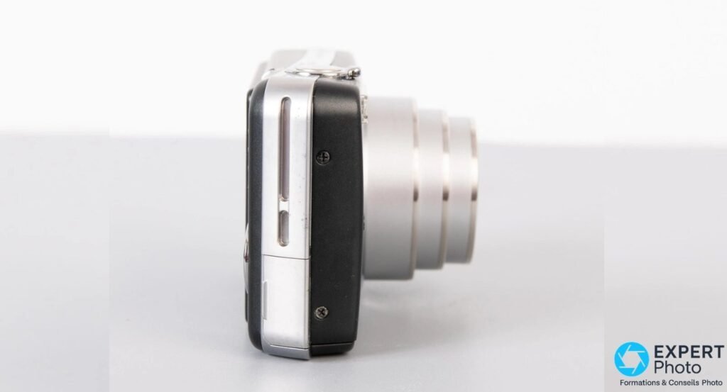 Ricoh Caplio R6 noir vu de profil opposé, trappe de connectique USB visible et objectif zoom déployé.