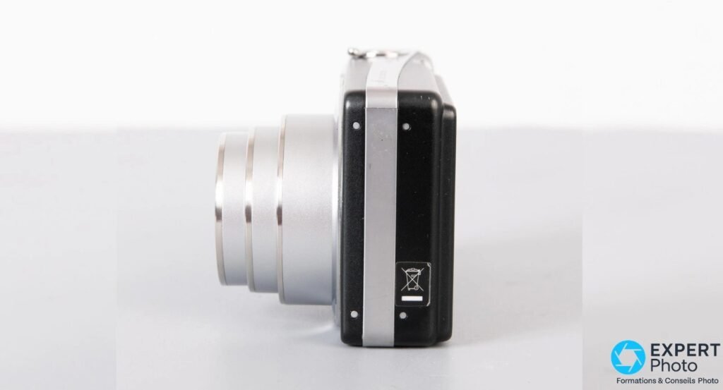 Ricoh Caplio R6 noir vu de profil avec objectif zoom 7,1x sorti, pictogramme de recyclage visible sur le flanc. 