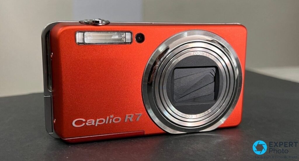 Ricoh Caplio R7 orange vu de face, objectif rétracté avec cache fermé, anneau argenté Ricoh Zoom Lens visible. 