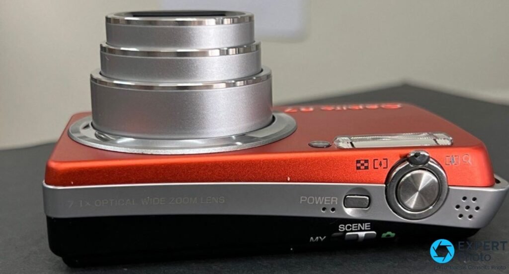 Ricoh Caplio R7 orange vu de dessus, objectif zoom déployé en trois sections, marquage 7.1x Optical Wide Zoom Lens lisible. 