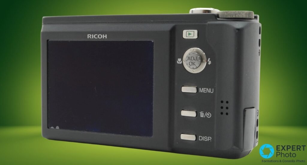 Face arrière du Ricoh Caplio R8 noir, écran LCD éteint, molette ADJ OK, boutons MENU et DISP, sur fond vert. 