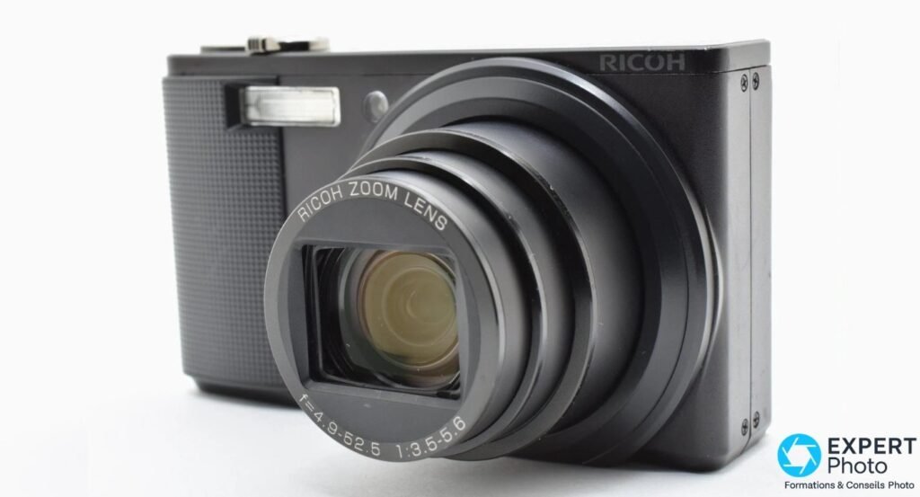 Ricoh CX2 noir vu de trois quarts avant, objectif zoom 28-300 mm complètement déployé, fond blanc studio.