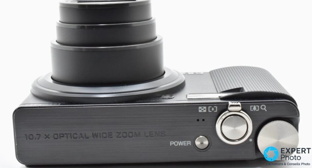 Vue de dessus du Ricoh CX2 avec objectif déployé et inscription gravée 10.7 X Optical Wide Zoom Lens.