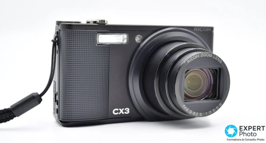 Ricoh CX3 vu de face en trois quarts avec zoom déployé, marquages RICOH, CX3 et RICOH ZOOM LENS visibles