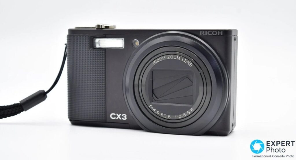 Ricoh CX3 vu de face en trois quarts avec zoom rétracté, RICOH, CX3 et f=4.9-52.5 1:3.5-5.6 visibles