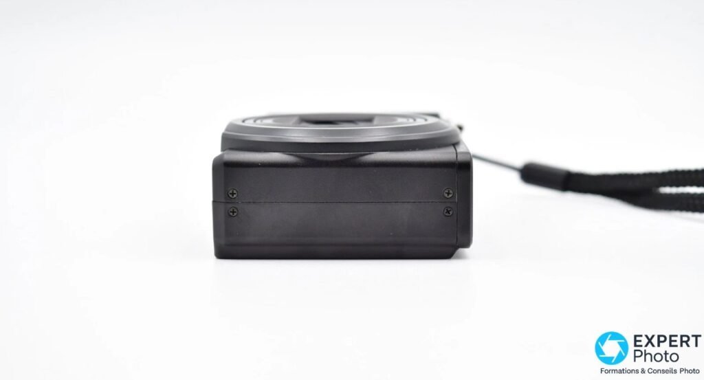 Ricoh CX3 vu de profil côté opposé, sans trappe, avec quatre vis visibles et dragonne noire à droite