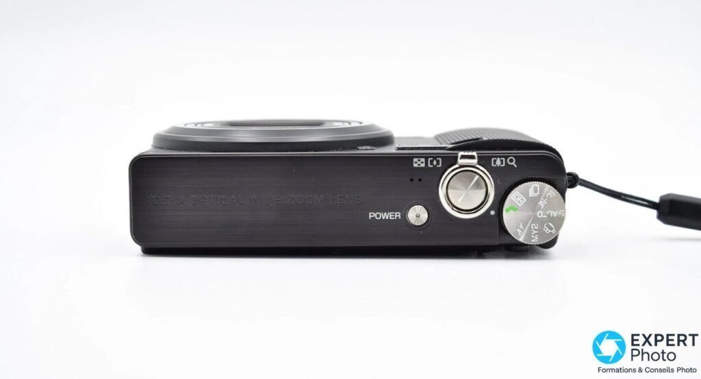 Vue de dessus du Ricoh CX3 avec mention 10.7x OPTICAL WIDE ZOOM LENS, bouton POWER, déclencheur et molette de modes