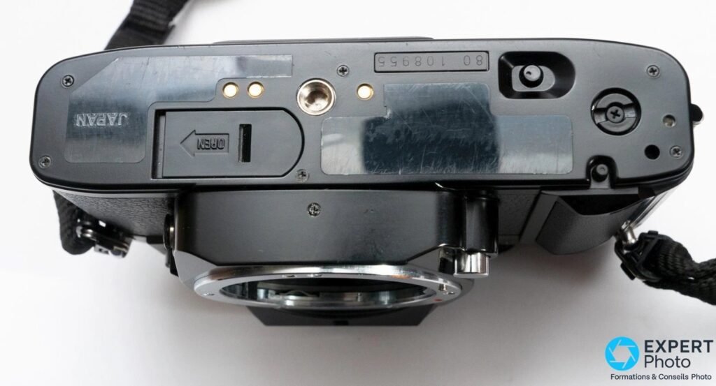 Dessous du Ricoh XR-P : trappe à piles OPEN, filetage trépied au centre et numéro de série sur plaque métallique