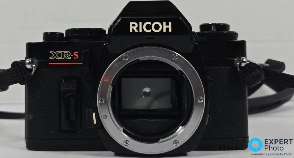 Boîtier Ricoh XR-S vu de face sans objectif, monture K chromée, logo RICOH sur le prisme et signature XR-S rouge.