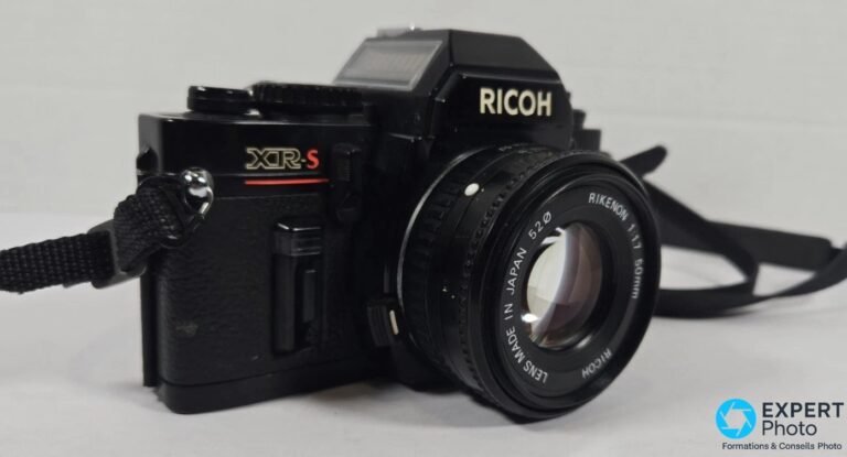 Reflex argentique Ricoh XR-S noir avec objectif Rikenon 50mm f/1.7 monté, vue 3/4 avant, signature XR-S rouge visible.