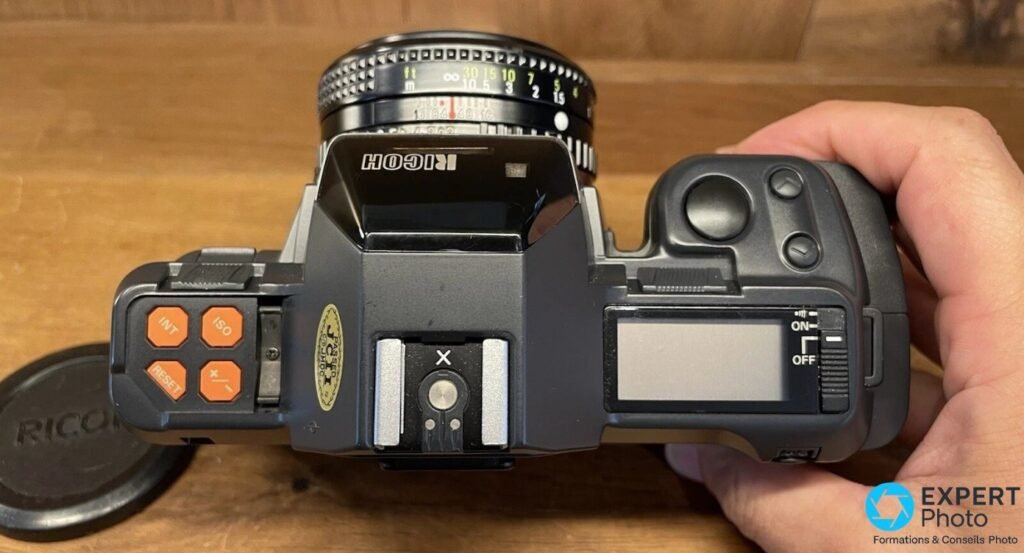  Vue de dessus du Ricoh XR-X tenu en main, boutons orange INT, ISO, RESET, +/-, griffe flash X et LCD ON/OFF