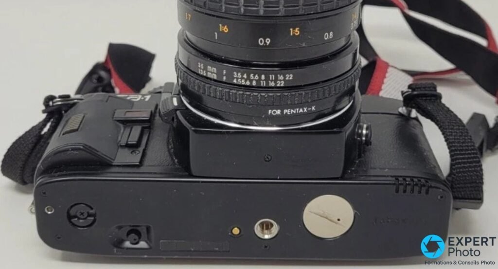 Sigma SA-1 vu de dessous, semelle avec filetage trépied, base d'un zoom 35-135 mm marqué FOR PENTAX-K.
